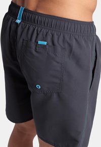 Bañador negro con cinturilla elástica, detalles en azul, un bolsillo trasero con botón y costuras en contraste.