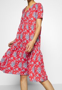 Robe florale rouge à manches courtes, décolleté en V, design à plusieurs niveaux, ornée de motifs floraux bleus et blancs, en tissu léger.