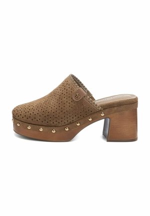 Bruine suède klomp met perforatiedesign, ronde neus en gouden studs langs de zool. Heeft een blokhak en een metallic accent.