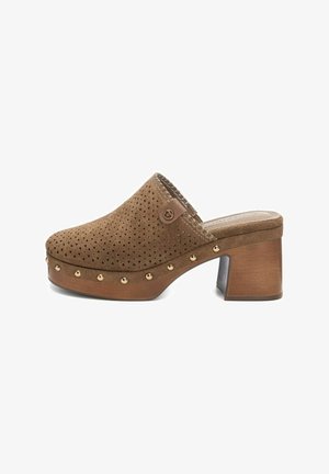 Zoccolo in suede marrone con design perforato, punta rotonda e borchie dorate lungo la suola. Presenta un tacco a blocco e un accento metallico.