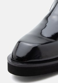 Fekete, fényes bőrből készült cipő, sima, lekerekített orral és vastag fekete gumitalppal, amely fényes bevonattal és sima textúrával rendelkezik.