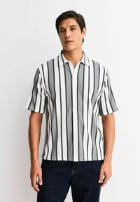 Short-sleeve button-up shirt featuring vertical black and white stripes, a collared neckline, and a textured fabric. Worn with dark jeans.