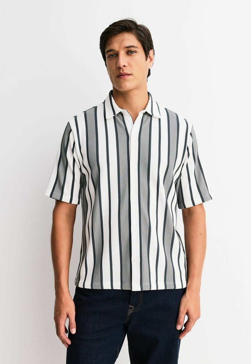 Short-sleeve button-up shirt featuring vertical black and white stripes, a collared neckline, and a textured fabric. Worn with dark jeans.