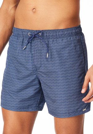 Man die blauwe zwemshorts draagt met een wit geometrisch patroon en een koordje aan de voorkant, weergegeven van taille tot midden van het bovenbeen.