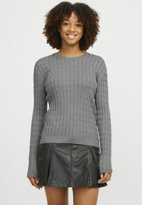 Maglione grigio a maglia con maniche lunghe, scollo rotondo e orlo a costine abbinato a una gonna nera in pelle sintetica con pieghe.