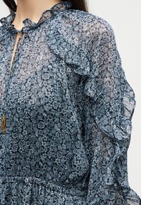 Διάφανη μπλε floral μπλούζα με βολάν στις μανσέτες και το ντεκολτέ, με κλείσιμο με κορδόνι και χρυσές χάντρες.