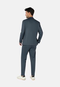 Maßgeschneiderter Herrenanzug aus strukturiertem, dunkelblauem Stoff; schlanke Passform mit einem einzelnen Schlitz hinten, kombiniert mit weißen Sneakern.