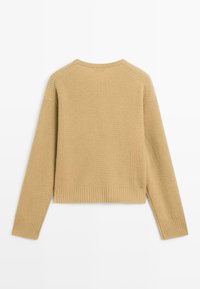Maglione beige a coste con maniche lunghe, scollo rotondo e vestibilità corta. Presenta una texture sottile e polsini e orlo elasticizzati.