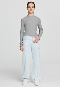 Maglietta grigia a maniche lunghe con spalle scoperte, abbinata a jeans a gamba larga blu chiaro con leggere decorazioni. Sneakers bianche completano l'outfit.