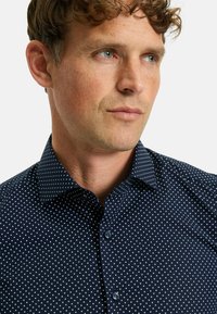 Donkerblauwe shirt met witte stippen, met knoopsluiting en normale pasvorm. Gladde stof met subtiele textuur, voorzien van twee knopen aan de voorkant.