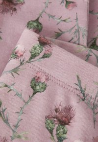 Bloemenstof in zachtroze met distelmotieven in groen en paars. Gladde textuur met zichtbare stiksels langs de randen.