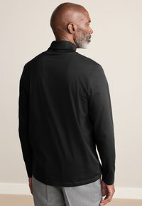 Sort langærmet skjorte med høj krave, glat tekstur og afslappet pasform. Vist bagfra, med minimal syning.