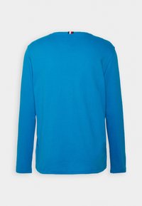 Langarm-T-Shirt aus leuchtend blauer Baumwolle. Verfügt über einen runden Halsausschnitt und einen kleinen dreifarbigen Streifen am Nacken.