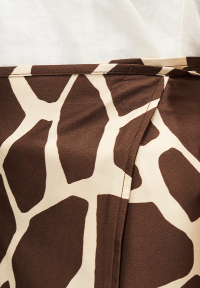 Κοντινό πλάνο σε ύφασμα με καφέ και μπεζ σχέδιο καμηλοπάρδαλης, με ορατή ραφή και διπλωμένη άκρη σε ανοιχτό φόντο.