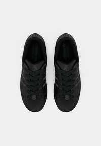 Black leather sneakers with a textured shell toe, featuring black laces and three side stripes. Logo embossed on tongue and side.