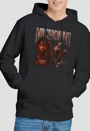 Schwarzer Kapuzenpullover mit dem Text "Michonne" und drei grafischen Bildern einer Frau, die ein Katana hält, kombiniert mit blauen Jeans.