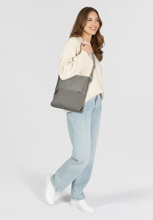 Borsa a spalla grigia realizzata in materiali lisci e testurizzati, con tasca frontale e tracolla regolabile. Indossata da una persona con un maglione chiaro e jeans.