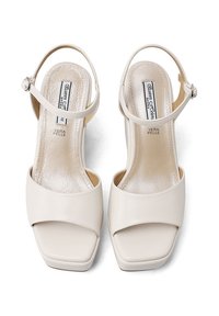 Sandali alti in pelle crema con punta quadrata, cinturini alla caviglia e texture liscia e lucida. Nome del marchio visibile sulle sole interne.