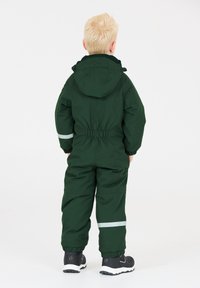 Groen waterdichte overall met een capuchon, elastische taille en reflecterende randen; gedragen met zwarte schoenen met witte zolen en accenten.