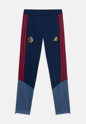 Granatowe spodnie treningowe FC Bayern Monachium z czerwonymi bocznymi paskami, złotymi logo, szarymi dolnymi częściami nogawek i suwakami przy kostkach.