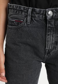 Černé džínové kalhoty s pěti kapsami, kovovým zapínáním na knoflík a jemným pruhovaným designem na kapsičce.