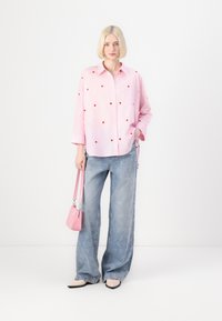 Light pink button-up shirt with red heart patterns, paired with wide-leg blue jeans featuring heart embroidery. Accessories include a small pink handbag.
