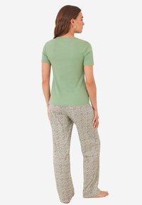 T-shirt vert à côtes et à manches courtes associé à un pantalon gris clair avec un petit motif floral noir, vu de dos.