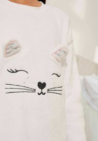 Hvid sweatshirt med et katteansigt design, der har sorte whiskers og en hjerteformet næse; inkluderer strukturerede, fluffy ører med lyserøde accenter.