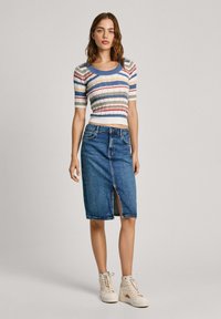 Stripet, ribstrikket top i blå, gul og rød. Højtaljet blå denimnederdel med slit foran. Modellen har beige høj top sneakers på.