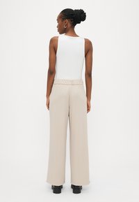 Λευκό αμάνικο τοπ σε συνδυασμό με μπεζ παντελόνι με φαρδιά μπατζάκια και ελαστική ζώνη στη μέση, φορεμένα με μαύρα μποτάκια στον αστράγαλο, φωτογραφημένα από πίσω.