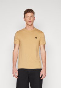 Kortærmet, rundhalset t-shirt i lysebrun bomuld, med et lille sort trælogo på venstre brystområde.