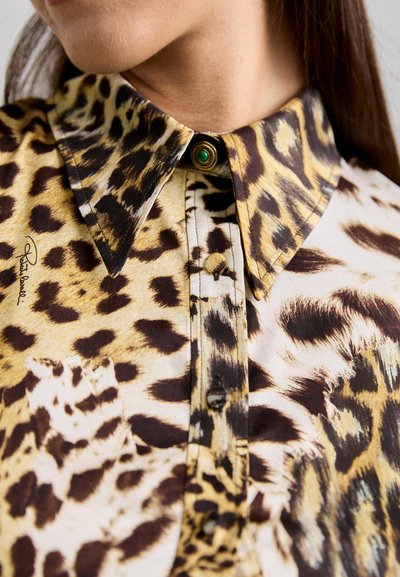 Leopard print blouse featuring a collar, green accent button, and fabric with smooth texture. Includes a chest pocket and button placket.