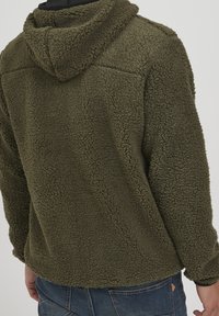 Olijfgroene fleece jack met een textuur, pluche oppervlak, capuchon en een ontspannen pasvorm. Beschikt over een rechte zoom en lange mouwen.
