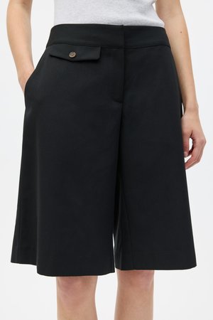 Pantaloni scurți negri croiți, fabricați din material țesut, cu un buzunar frontal cu nasture, față plată și croială lejeră care ajunge până la mijlocul coapsei.