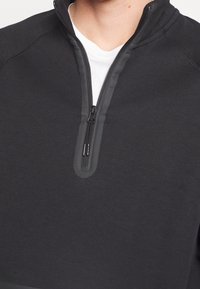 Sudadera negra de media cremallera con una textura suave, cuello alto y detalles de cremallera en contraste. Diseñada para la comodidad y el uso casual.