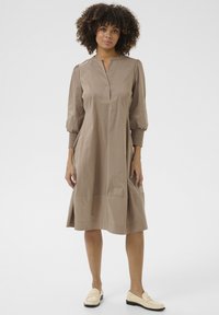 Helepruun, põlvikuni ulatuv kleit, millel on lihtne nööpide rida, puffsleevid ja mugav lõige. Sile puuvillane kangas, millel on peen sära.