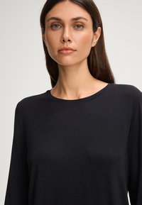 Zwarte langslijpste top met een ronde hals, gemaakt van een gladde stof. Minimalistisch ontwerp en fitte silhouet zonder patronen of accenten.