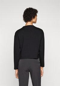 Μαύρο κοντό φούτερ με μακριά μανίκια, διαθέτει στρογγυλή λαιμόκοψη και λεία υφή, συνδυασμένο με γκρίζες εφαρμοστές παντελόνες.