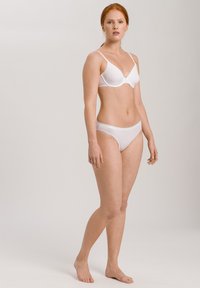 Reggiseno bianco con coppe senza cuciture e spalline regolabili, abbinato a slip bianchi a vita bassa. Tessuto liscio, design minimalista e costruzione essenziale.