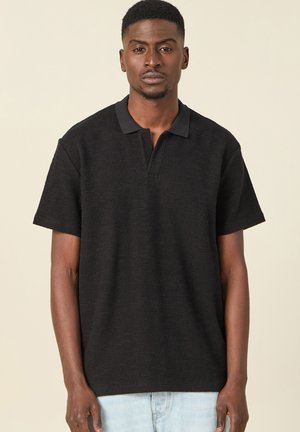 Camisa polo negra, tela texturizada, mangas cortas y un cuello negro en contraste. Presenta una abertura frontal de media botonadura.