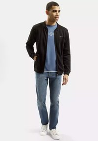 Czarna kurtka zapinana na zamek, na niebieskiej koszuli, w połączeniu z jasnoniebieskimi dżinsami i białymi trampkami. Gładkie faktury i luźny krój.