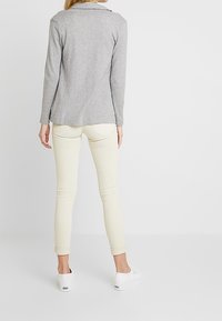 Maglia grigia a maniche lunghe con colletto, abbinata a jeans skinny chiari e sneakers bianche. Il tessuto appare liscio; design minimalista.