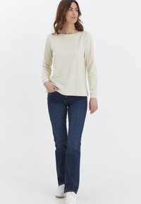 Sudadera de color crema claro con el texto "PASIÓN", combinada con jeans de campana de color azul oscuro y zapatillas blancas. Textura suave, ajuste informal, mangas largas.