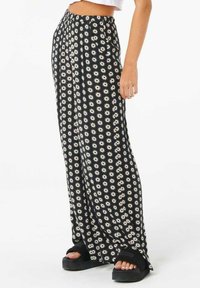 Pantaloni neri fluenti con un motivo floreale bianco, caratterizzati da una vestibilità comoda e una vita elastica. Indossati con sandali neri spessi.