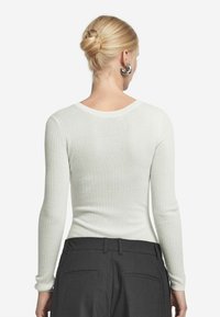 Vit ribbad långärmad topp med rund halsringning, texturerad tyg och slim fit. Bärs tillsammans med mörka byxor, vilket framhäver bakvyn.