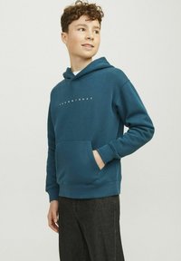 Sudadera con capucha en color verde azulado, hecha de una tela suave. Tiene un bolsillo frontal y un logo impreso en blanco. Puños y cintura acanalados. Corte casual.