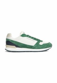 Baskets basses blanches et vertes avec détails en daim, marquées « Tommy Hilfiger » sur le côté, avec une semelle blanche rembourrée et une semelle extérieure foncée.