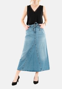 Denim maxi-rok met een trekkoord in de taille, voorzien van een voornaad en een lichtblauwe wassing. Gecombineerd met een zwart mouwloos topje en hakken.