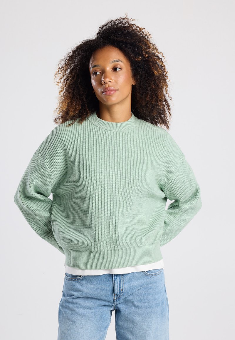 Mint green knitted sweater with ribbed texture, round neckline, and dropped shoulders, paired with light blue jeans.