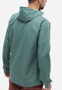 Veste à capuche vert clair en tissu lisse et résistant à l'eau, présentant une coupe décontractée et des manches longues, avec une poche zippée sur le côté.